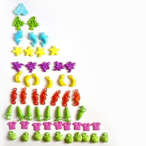 May include: A colorful assortment of plastic buttons in a rainbow pattern, including cars, trees, stars, dolphins, butterflies, bananas, seahorses, umbrellas, shirts, and apples.