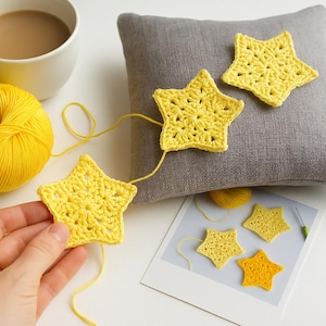 May include: Handmade yellow crochet stars, some strung together, others on a grey cushion. A ball of yellow yarn, a cup of coffee, and a crochet hook are also visible. The stars are likely part of a crafting project.