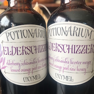 May include: Two dark glass bottles with black caps and white labels. The labels read "POTIONARIUM ELDERSCHIZZER" and list ingredients like elderberry, schisandra, and honey. The bottles are filled with a dark liquid.