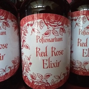 May include: Several dark glass bottles with black caps. Each bottle has a white label with red floral designs and the words "Potionarium Red Rose Elixir". The labels are slightly curved to fit the bottle shape.