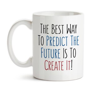 May include: White ceramic mug with a curved handle. The mug features the text "THE BEST WAY TO PREDICT THE FUTURE IS TO CREATE IT!" in black, blue, and red lettering. The mug is designed for hot beverages.