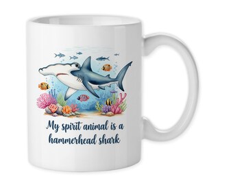 May include: White ceramic mug featuring a colorful illustration of a hammerhead shark swimming in the ocean. The design includes coral, fish, and the text "My spirit animal is a hammerhead shark."
