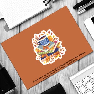 May include: A sticker featuring a blue and white coffee mug with a stack of books and autumn leaves. The text "Please Note: Decal Sticker Size is Dependent Upon Your Choice. Multiple Decal Sticker Sizes Are Available." is at the bottom of the sticker.