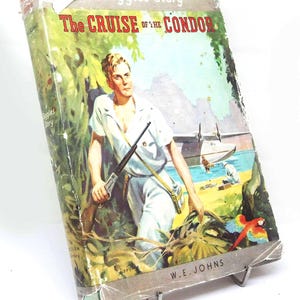 May include: A vintage hardback book titled A Biggles Story The Cruise of the Condor by W.E. Johns. The cover features a colour illustration of a person in white clothing holding a rifle in a jungle setting with a seaplane and a colourful parrot.