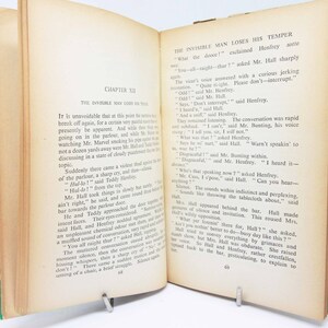 Op de afbeelding: Een open oud boek met vergeelde pagina's. De tekst, getiteld "The Invisible Man Loses His Temper", is zichtbaar. Een metalen clip houdt de pagina's open, met een groene rug en randen.