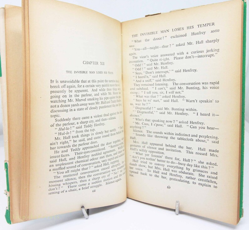 Op de afbeelding: Een open oud boek met vergeelde pagina's. De tekst, getiteld "The Invisible Man Loses His Temper", is zichtbaar. Een metalen clip houdt de pagina's open, met een groene rug en randen.