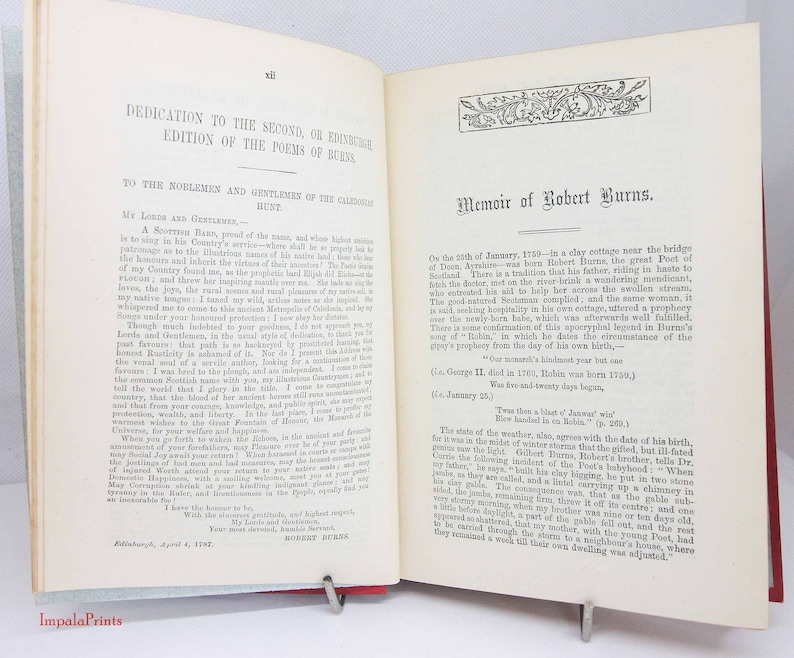 Pode incluir: Um livro antigo aberto com p&aacute;ginas cor de creme e texto impresso em preto. A p&aacute;gina esquerda intitula-se Dedication to the Second, or Edinburgh Edition of the Poems of Burns. A p&aacute;gina direita intitula-se Memoir of Robert Burns.