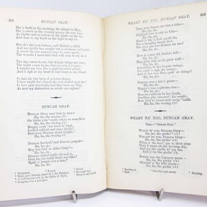Pode incluir: Um livro aberto com p&aacute;ginas cor de creme apresentando o texto impresso em preto do poema Duncan Gray e Weary Fa' You, Duncan Gray. As p&aacute;ginas est&atilde;o numeradas 302 e 303, com capas vermelhas vis&iacute;veis nas bordas e notas de rodap&eacute;.