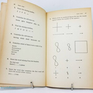 May include: Open book with pages displaying a test. The left page has numbered questions with fill-in-the-blank and odd-one-out problems. The right page has a matching shapes test. The book is held open by a metal clip.