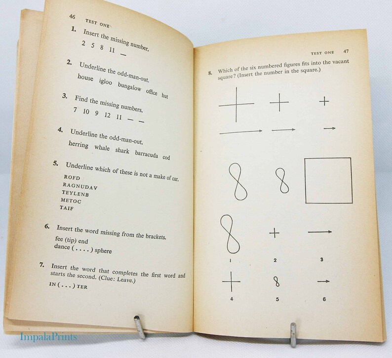 May include: Open book with pages displaying a test. The left page has numbered questions with fill-in-the-blank and odd-one-out problems. The right page has a matching shapes test. The book is held open by a metal clip.