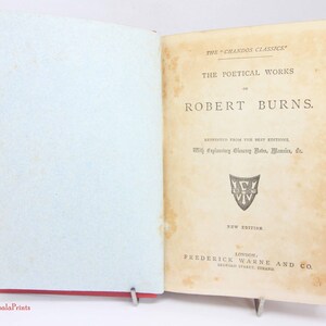 Pode incluir: Um livro antigo aberto intitulado The Poetical Works of Robert Burns da s&eacute;rie The Chandos Classics. A p&aacute;gina de t&iacute;tulo cor de creme apresenta texto preto, um pequeno emblema de escudo e os detalhes da editora Frederick Warne and Co. em Londres.