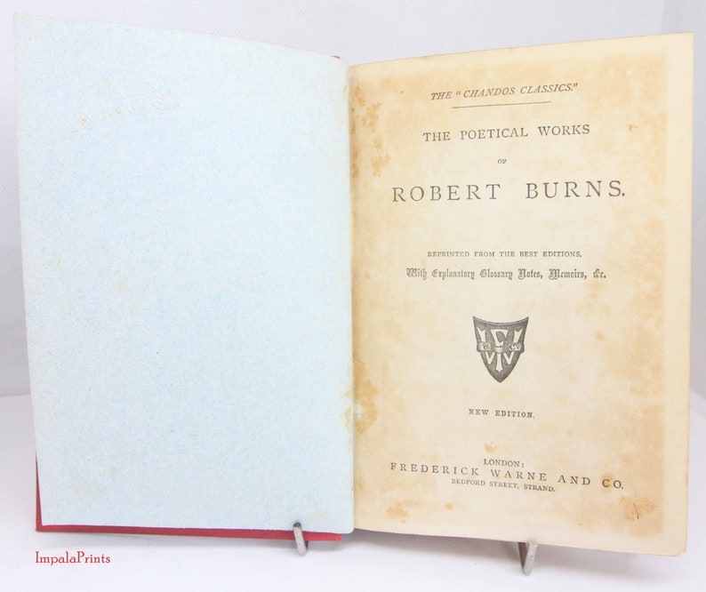 Pode incluir: Um livro antigo aberto intitulado The Poetical Works of Robert Burns da s&eacute;rie The Chandos Classics. A p&aacute;gina de t&iacute;tulo cor de creme apresenta texto preto, um pequeno emblema de escudo e os detalhes da editora Frederick Warne and Co. em Londres.