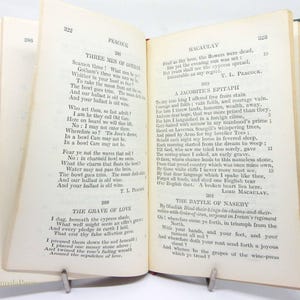 May include: An open book displaying poetry, including "Three Men of Gotham" and "The Grave of Love". The book has a green cover and is held open by a metal book holder. The pages are aged.