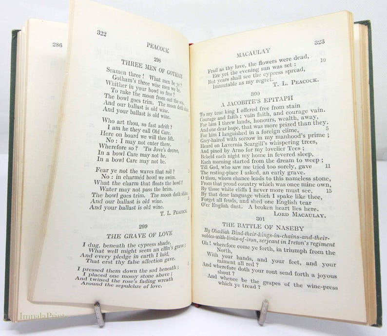 May include: An open book displaying poetry, including "Three Men of Gotham" and "The Grave of Love". The book has a green cover and is held open by a metal book holder. The pages are aged.