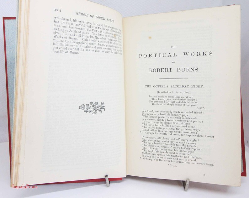Pode incluir: Um livro antigo aberto intitulado The Poetical Works of Robert Burns, com p&aacute;ginas cor de creme e texto impresso em preto. A p&aacute;gina esquerda mostra uma se&ccedil;&atilde;o de mem&oacute;rias com uma pequena ilustra&ccedil;&atilde;o floral, enquanto a p&aacute;gina direita exibe o poema The Cotter's Saturday Night.