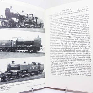 May include: An open book page featuring three black and white photographs of steam locomotives stacked vertically on the left side, with descriptive text titled THE TRACK on the right side, detailing railway maintenance and snow-plough operations.