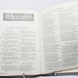 May include: An open book with a yellowed page, featuring a poem titled "Songs of Labour." The poem is about the dedication of workers in various professions, including shipbuilders, shoemakers, and farmers. The book is bound in red leather with gold accents.