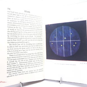 Puede incluir: Un libro abierto con el título "STARS" en la parte superior de la página. La página derecha muestra un diagrama de estrellas dentro de una cuadrícula, sobre un fondo azul oscuro. La imagen es de un libro de astronomía antiguo.