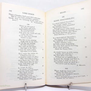 May include: An open book of poetry by Lord Byron and Keats, held open by a metal clip. The text is printed in black ink on off-white paper. The book has a green spine and the pages are aged.