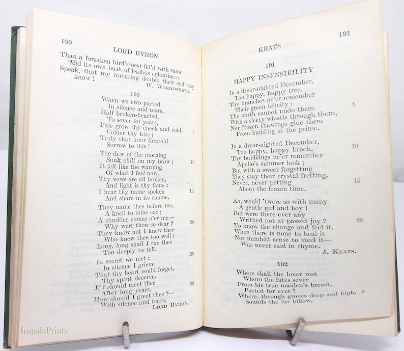 May include: An open book of poetry by Lord Byron and Keats, held open by a metal clip. The text is printed in black ink on off-white paper. The book has a green spine and the pages are aged.
