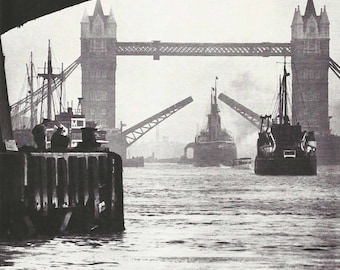 May include: Black and white photograph of the Tower Bridge in London, with the bascules raised. Several ships are in the water, and the bridge's towers are visible in the background. The image is taken from a low angle, looking up at the bridge.