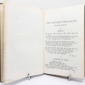 May include: An open book with the title "THE GOLDEN TREASURY BOOK FIRST" visible. The pages are aged, with black text. The book is held open by a metal clip. The text includes the poem "Spring" by T. Nash.