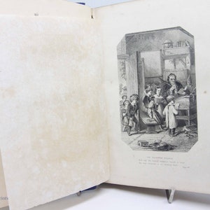 May include: A black and white illustration of a classroom scene with a teacher and students. The teacher is standing at a desk, and the students are sitting or standing around him. The illustration is from an old book.
