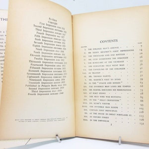 Op de afbeelding: Open boek met verouderde, vergeelde pagina's. De linkerpagina toont de drukgeschiedenis van het boek, terwijl de rechterpagina de inhoudsopgave weergeeft, met hoofdstuktitels zoals "The Strange Man's Arrival".