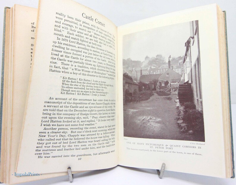 May include: An open book with text and a black and white photograph of a street scene. The text includes the title "Castle Corner" and the phrase "One of many picturesque & quaint corners in St. Peter Port."