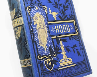 May include: A blue hardcover book titled The Lansdowne Poets Hood with gold foil detailing. The cover features a central illustration of a figure holding a lyre, surrounded by stars, floral motifs, and the text With Explanatory Notes.