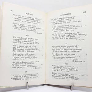 May include: An open book of poetry, with poems by Thomson and Goldsmith on facing pages. The book is held open by a metal book stand. The pages are aged and the text is in black.