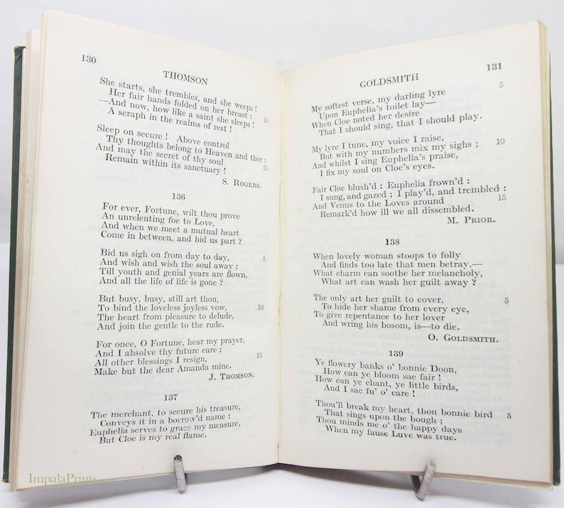 May include: An open book of poetry, with poems by Thomson and Goldsmith on facing pages. The book is held open by a metal book stand. The pages are aged and the text is in black.