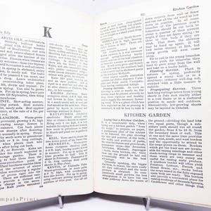 May include: Open book with text about gardening, including Kaffir Lily and Kitchen Garden. The pages are held open by a metal book stand. The text is in black font.