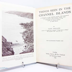 May include: Open book titled "Things Seen in the Channel Islands" by Clive Holland, published in 1929. The book features a black and white photograph of a coastal landscape and text describing the islands.