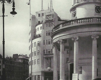 May include: A black and white photo of a building with a clock tower. The building has a modern design with large windows and a flat roof. The clock tower is a traditional design with a dome and columns. The building is located in a city and there are other buildings in the background.