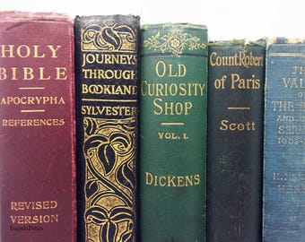 May include: A row of five antique hardcover books with visible spines. The books are colored maroon, black, green, dark gray, and blue. The titles include Holy Bible, Journeys Through Bookland, Old Curiosity Shop, Count Robert of Paris, and The Value of the Bible.