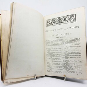 May include: An open book with a brown leather cover and yellowed pages. The text on the page reads "Whittier's Poetical Works. Indian Legends. Part I. Mogg Megone."