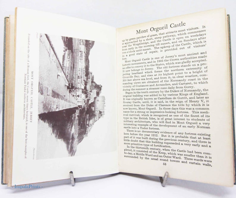 May include: Open book with a black and white photo of Mont Orgueil Castle, Jersey. Text on the right describes the castle's history and features. The book is held open by a metal book stand.