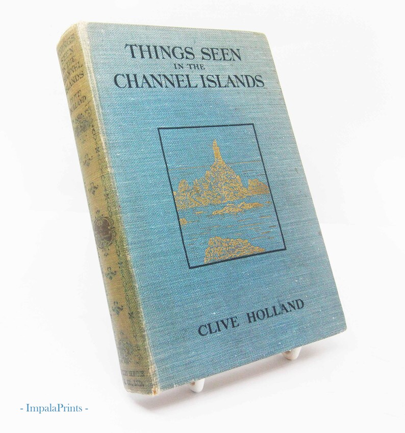 May include: A vintage book titled "Things Seen in the Channel Islands" by Clive Holland. The book has a light blue cover with gold lettering and a gold illustration. The spine is a faded gold color.