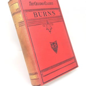 May include: A hardback book titled The Chandos Classics BURNS with a bright red front cover featuring black decorative lines and a small shield emblem. The spine is a faded tan colour with gold lettering and black horizontal border details.