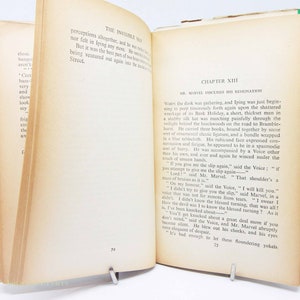 Op de afbeelding: Open boek met tekst uit "De onzichtbare man" van H.G. Wells. De pagina's zijn vergeeld met zichtbare tekst. Het boek wordt opengehouden door een metalen boekensteun. De kaft van het boek is groen.