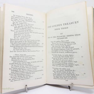 May include: An open book with a green cover, featuring text from "The Golden Treasury, Book Third." The pages display poetry by Dryden. A metal book stand holds the book open.