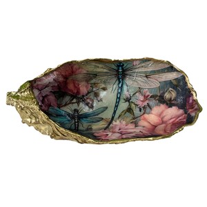 May include: An oyster shell dish featuring a decoupage design of two blue dragonflies surrounded by pink and dark red floral blooms. The interior surface is decorated with the botanical print, while the outer edges are finished with a metallic gold trim.