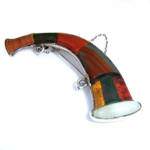 May include: A silver brooch shaped like a horn, with a multi-colored agate stone inlay. The brooch has a chain attached to the top.