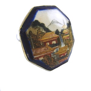 Op de afbeelding: Achtkantige broche van blauw en wit porselein met een gouden sc&egrave;ne van een Japans berglandschap met pagodes en een waterval.