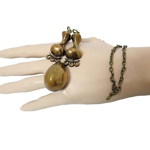 May include: A gold-toned necklace with a large teardrop-shaped pendant and two smaller teardrop-shaped charms. The necklace is made of a chain link style.