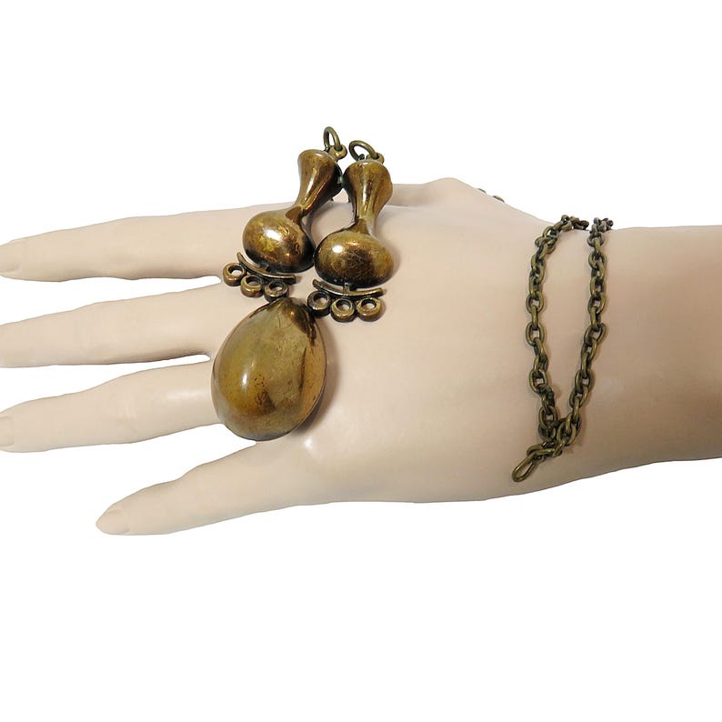 May include: A gold-toned necklace with a large teardrop-shaped pendant and two smaller teardrop-shaped charms. The necklace is made of a chain link style.