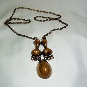 May include: A bronze necklace with a pendant featuring two teardrop-shaped charms and a larger oval-shaped charm.
