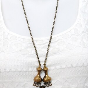May include: A gold-toned necklace with a unique pendant featuring two teardrop-shaped pieces connected by a smaller teardrop. The pendant hangs from a delicate chain.