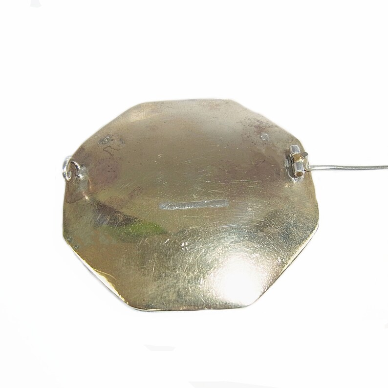 Op de afbeelding: Een zilveren achthoekige broche met een pin aan de achterkant. De broche heeft een glad, licht getextureerd oppervlak en is gemarkeerd met de letters "R" en "S".